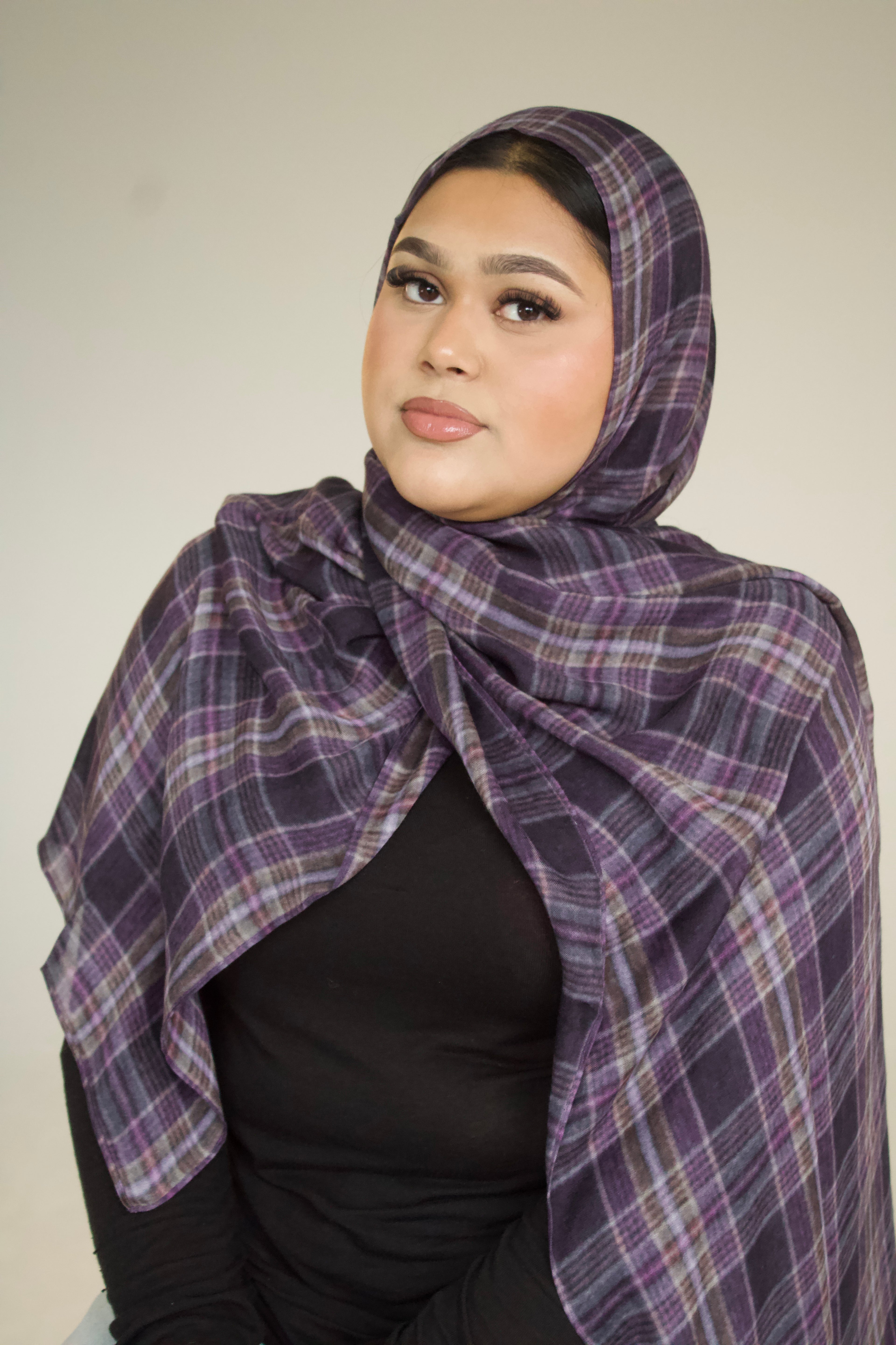 Woman wearing a purple plaid headscarf against a plain background